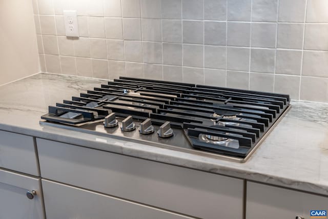 room details with decorative backsplash, light stone countertops, and stainless steel gas cooktop