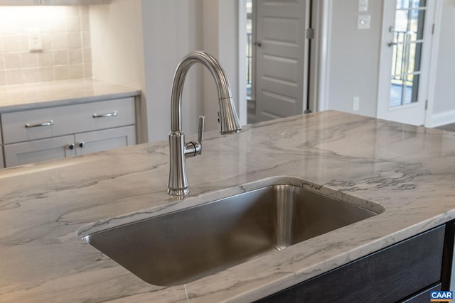 details featuring tasteful backsplash, white cabinets, light stone counters, and a sink