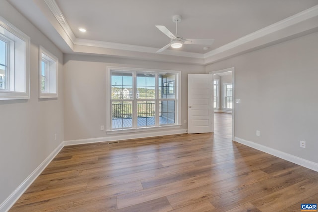 empty room featuring plenty of natural light, ornamental molding, a tray ceiling, and wood finished floors