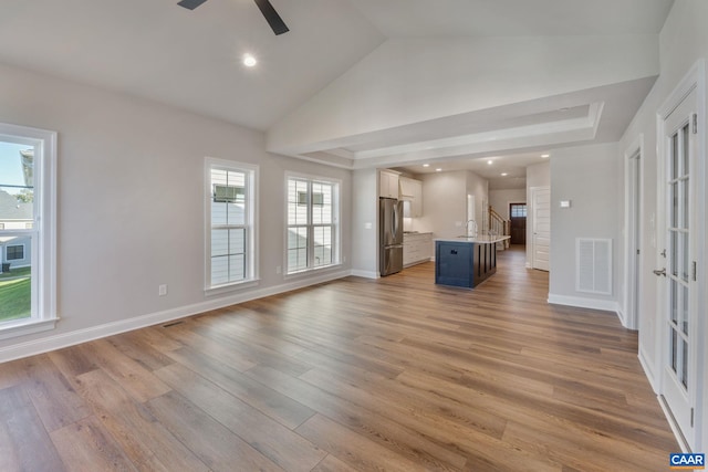 unfurnished living room with visible vents, baseboards, ceiling fan, light wood-type flooring, and a sink