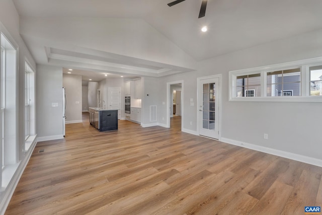 unfurnished living room with baseboards, ceiling fan, lofted ceiling, light wood-style floors, and a sink