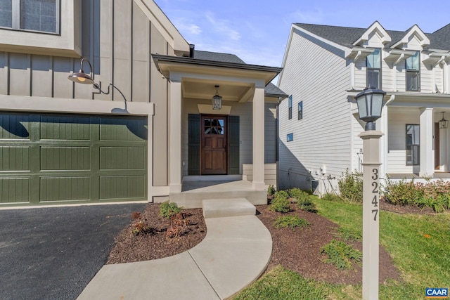 entrance to property with board and batten siding, an attached garage, and driveway