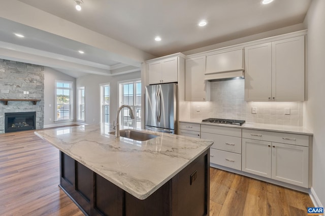 kitchen with light stone countertops, light wood finished floors, a sink, appliances with stainless steel finishes, and tasteful backsplash