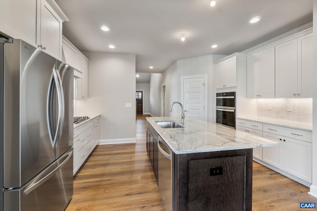 kitchen featuring a kitchen island with sink, light wood-style flooring, a sink, stainless steel appliances, and decorative backsplash