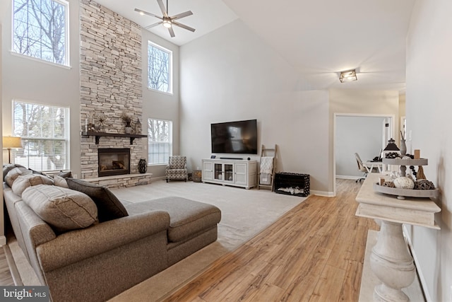 living area with baseboards, ceiling fan, a stone fireplace, a high ceiling, and wood finished floors