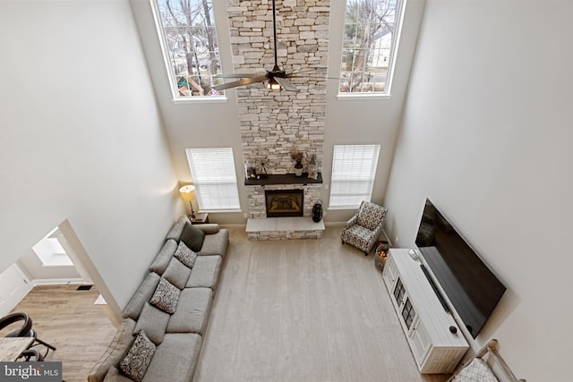 living area with plenty of natural light, a stone fireplace, ceiling fan, and a towering ceiling