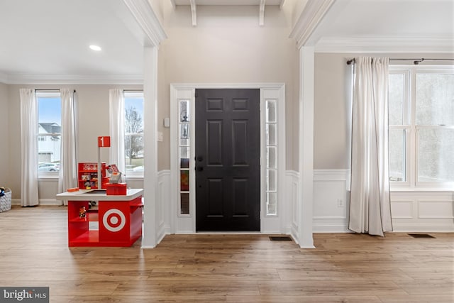 foyer with crown molding, a decorative wall, wood finished floors, and wainscoting