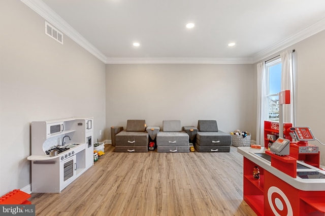 recreation room featuring visible vents, light wood-type flooring, baseboards, and ornamental molding