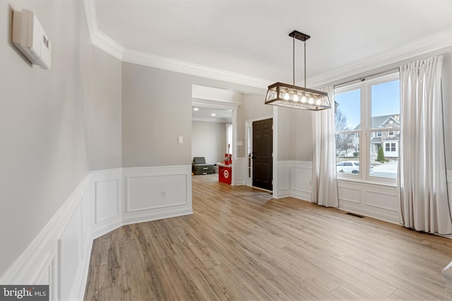 unfurnished dining area with a decorative wall, visible vents, ornamental molding, and light wood finished floors