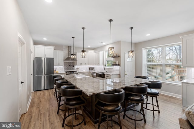 kitchen featuring light wood finished floors, backsplash, appliances with stainless steel finishes, wall chimney exhaust hood, and a sink