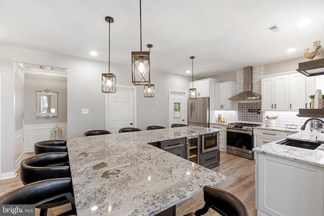 kitchen with a kitchen breakfast bar, wall chimney range hood, appliances with stainless steel finishes, and a sink