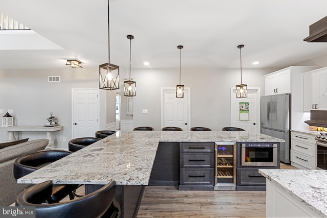 kitchen featuring light wood finished floors, visible vents, appliances with stainless steel finishes, a kitchen breakfast bar, and white cabinetry