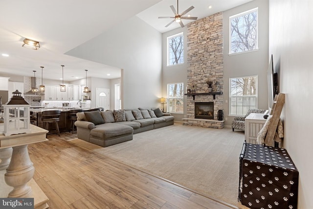 living area featuring recessed lighting, light wood-style floors, a stone fireplace, and ceiling fan