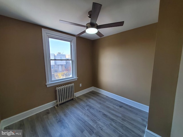 spare room featuring ceiling fan, radiator, baseboards, and wood finished floors