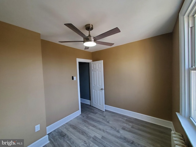 spare room with radiator, baseboards, ceiling fan, and wood finished floors