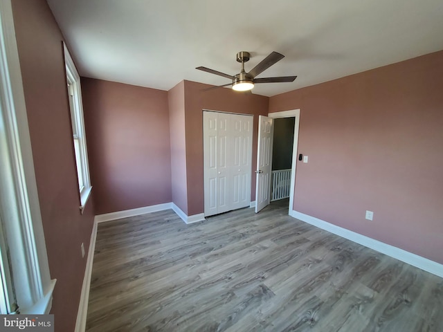 unfurnished bedroom featuring a closet, baseboards, wood finished floors, and a ceiling fan