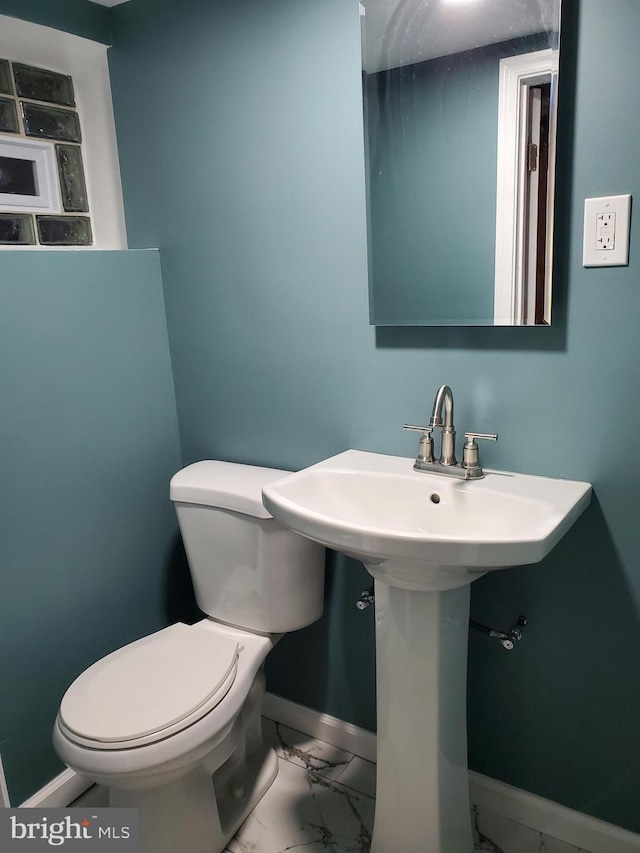 bathroom with marble finish floor, toilet, baseboards, and a sink