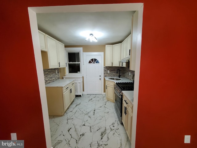 kitchen featuring marble finish floor, a sink, light countertops, decorative backsplash, and stainless steel range with gas stovetop