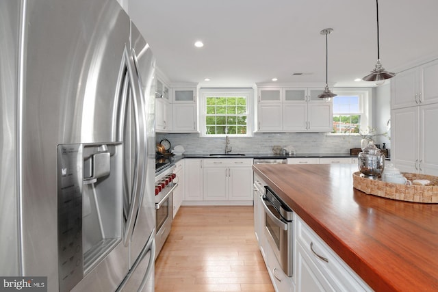 kitchen featuring wooden counters, glass insert cabinets, decorative backsplash, stainless steel appliances, and a sink