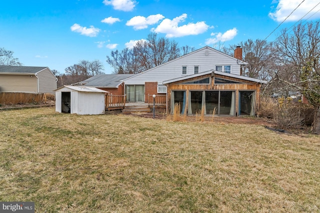 rear view of house featuring an outbuilding, fence, a wooden deck, a chimney, and a lawn