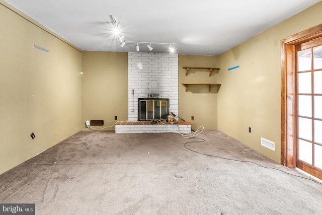 unfurnished living room featuring carpet flooring, a brick fireplace, rail lighting, and visible vents