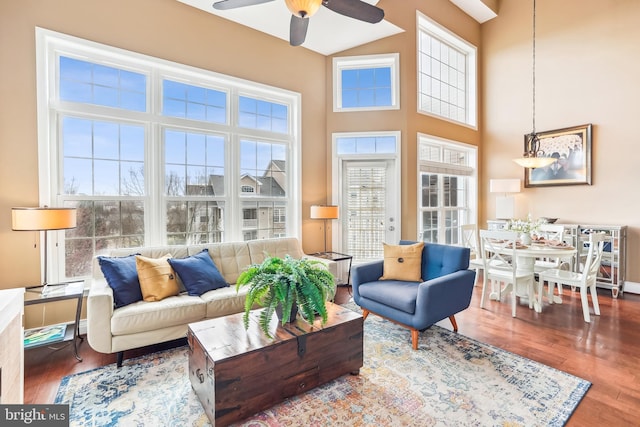 living area with a towering ceiling, a ceiling fan, and wood finished floors