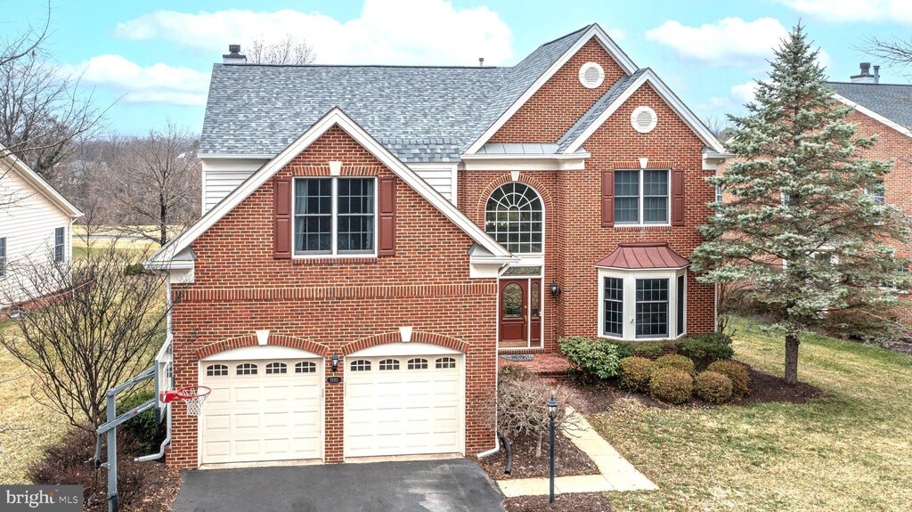 traditional-style home featuring driveway, a shingled roof, a front yard, an attached garage, and brick siding