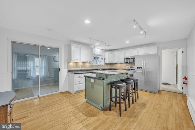 kitchen featuring a kitchen island, a breakfast bar, light wood-style flooring, stainless steel appliances, and white cabinetry