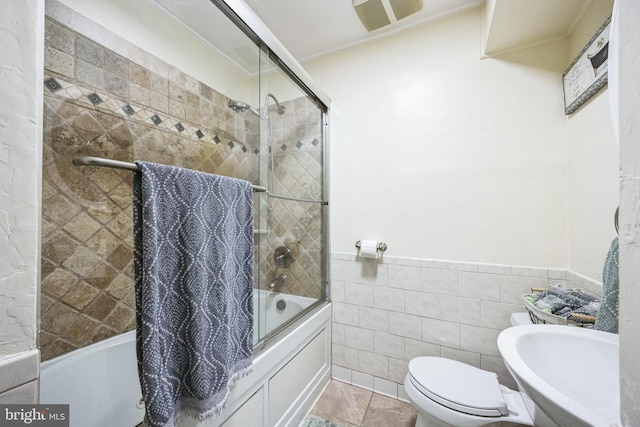 full bathroom featuring bath / shower combo with glass door, toilet, wainscoting, tile walls, and a sink