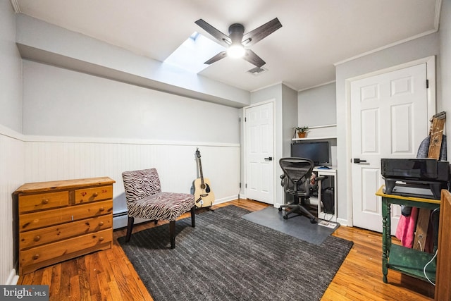 sitting room featuring visible vents, wood finished floors, a wainscoted wall, and ceiling fan