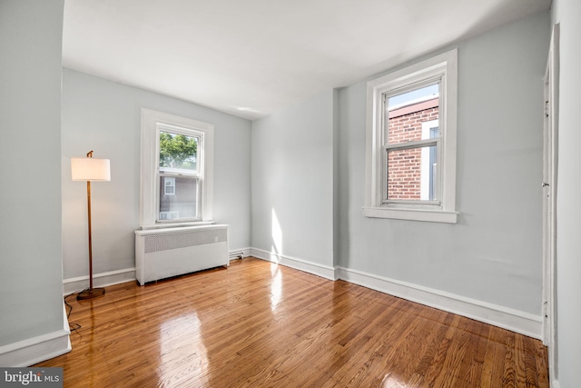 spare room with baseboards, wood finished floors, and radiator heating unit