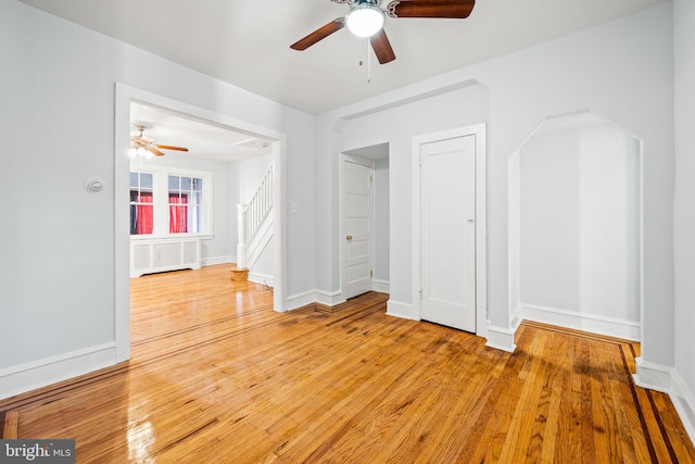 empty room with arched walkways, stairway, ceiling fan, and hardwood / wood-style floors