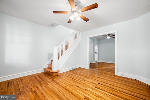 unfurnished living room with stairs, baseboards, light wood finished floors, and ceiling fan