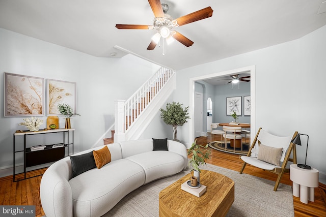 living room with baseboards, ceiling fan, stairway, wood finished floors, and arched walkways