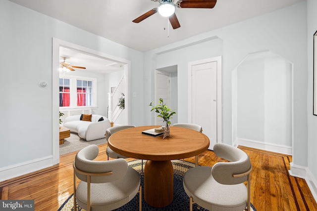 dining space featuring stairs, baseboards, wood finished floors, and a ceiling fan