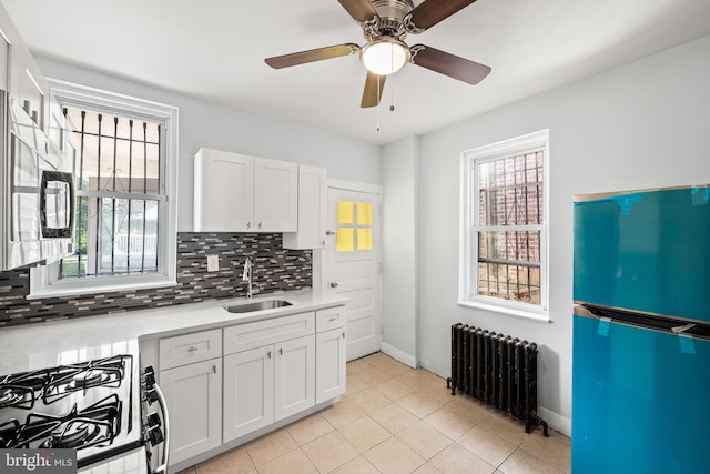 kitchen featuring tasteful backsplash, radiator, range with gas cooktop, freestanding refrigerator, and a sink