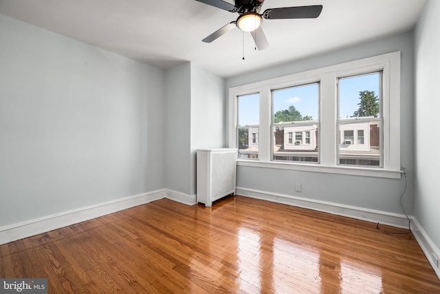 spare room featuring baseboards, a ceiling fan, wood finished floors, and radiator heating unit