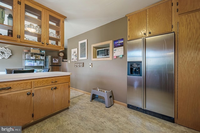 kitchen with brown cabinetry, baseboards, light countertops, glass insert cabinets, and built in refrigerator