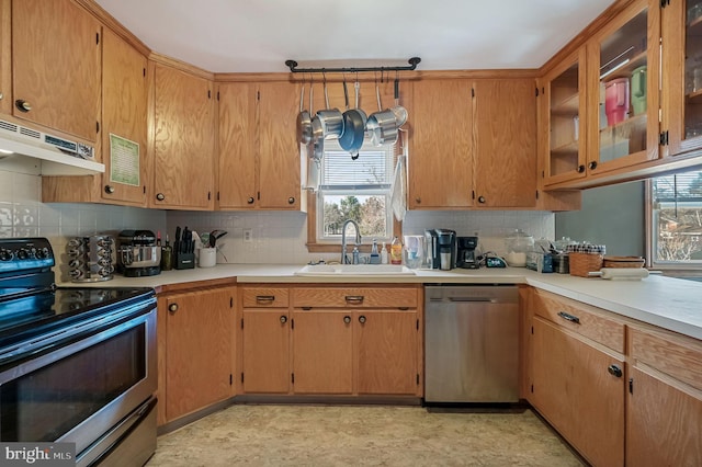 kitchen with a sink, light countertops, under cabinet range hood, appliances with stainless steel finishes, and tasteful backsplash