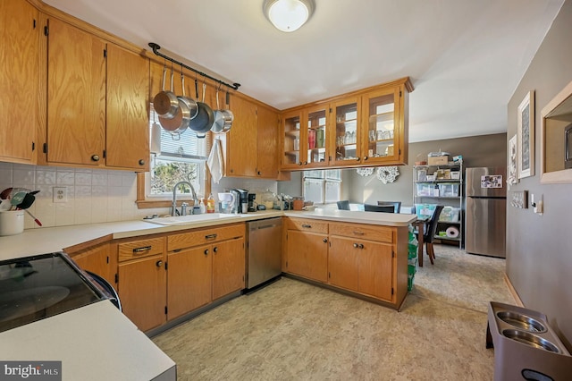 kitchen with backsplash, light countertops, a peninsula, stainless steel appliances, and a sink