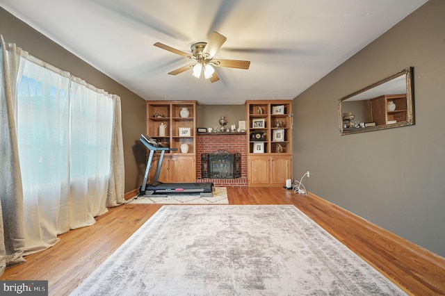 exercise room with baseboards, a brick fireplace, wood finished floors, and a ceiling fan