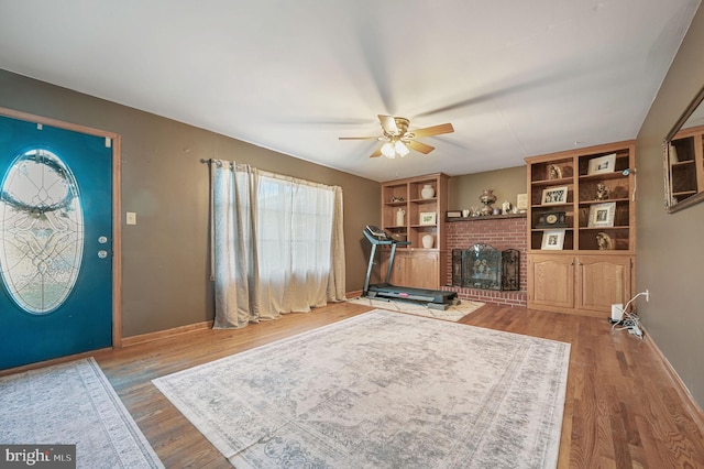 entryway featuring a brick fireplace, wood finished floors, baseboards, and ceiling fan