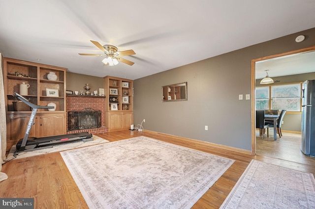 living area with a fireplace, wood finished floors, baseboards, and ceiling fan