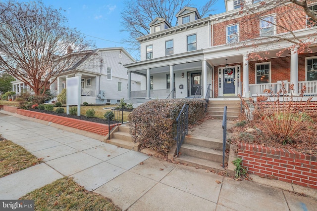 view of front of house featuring mansard roof, brick siding, and a porch