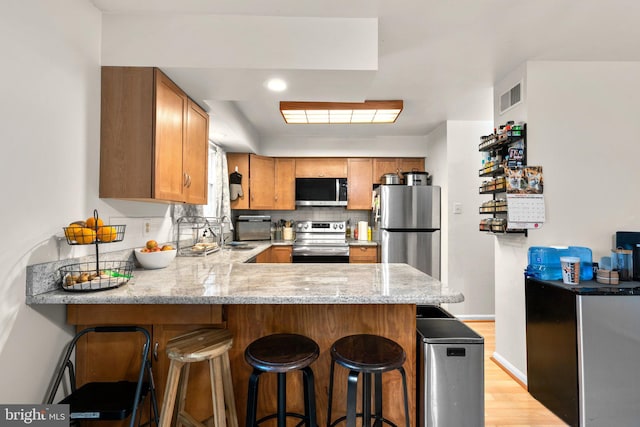 kitchen featuring tasteful backsplash, visible vents, a peninsula, brown cabinetry, and stainless steel appliances