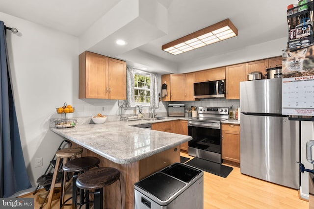 kitchen with light wood-type flooring, a sink, a kitchen breakfast bar, appliances with stainless steel finishes, and a peninsula