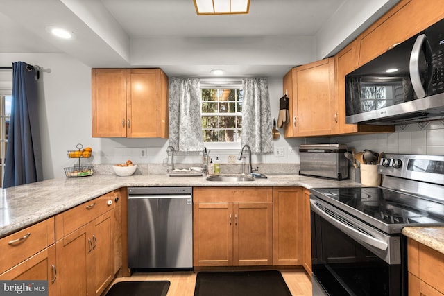 kitchen with a sink, light stone counters, backsplash, stainless steel appliances, and light wood-style floors