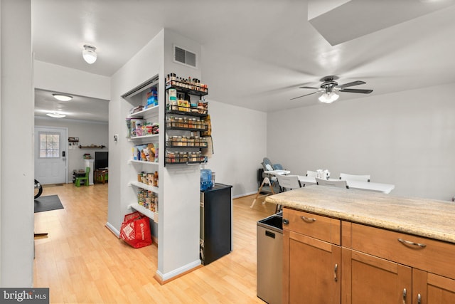 kitchen with visible vents, light wood finished floors, brown cabinetry, light countertops, and ceiling fan