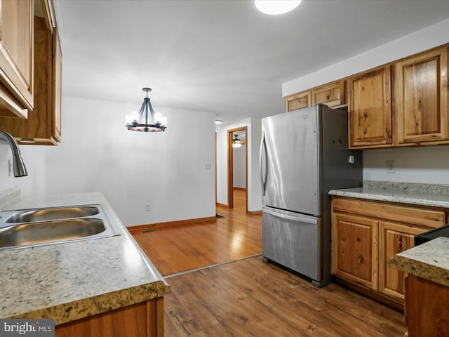 kitchen featuring dark wood-style floors, brown cabinets, freestanding refrigerator, and a sink