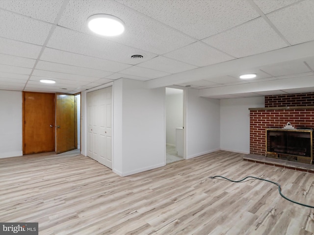 finished basement with a drop ceiling, visible vents, wood finished floors, and a fireplace